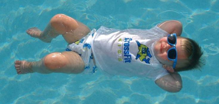 A baby in sunglasses floating happily in a sunlit pool