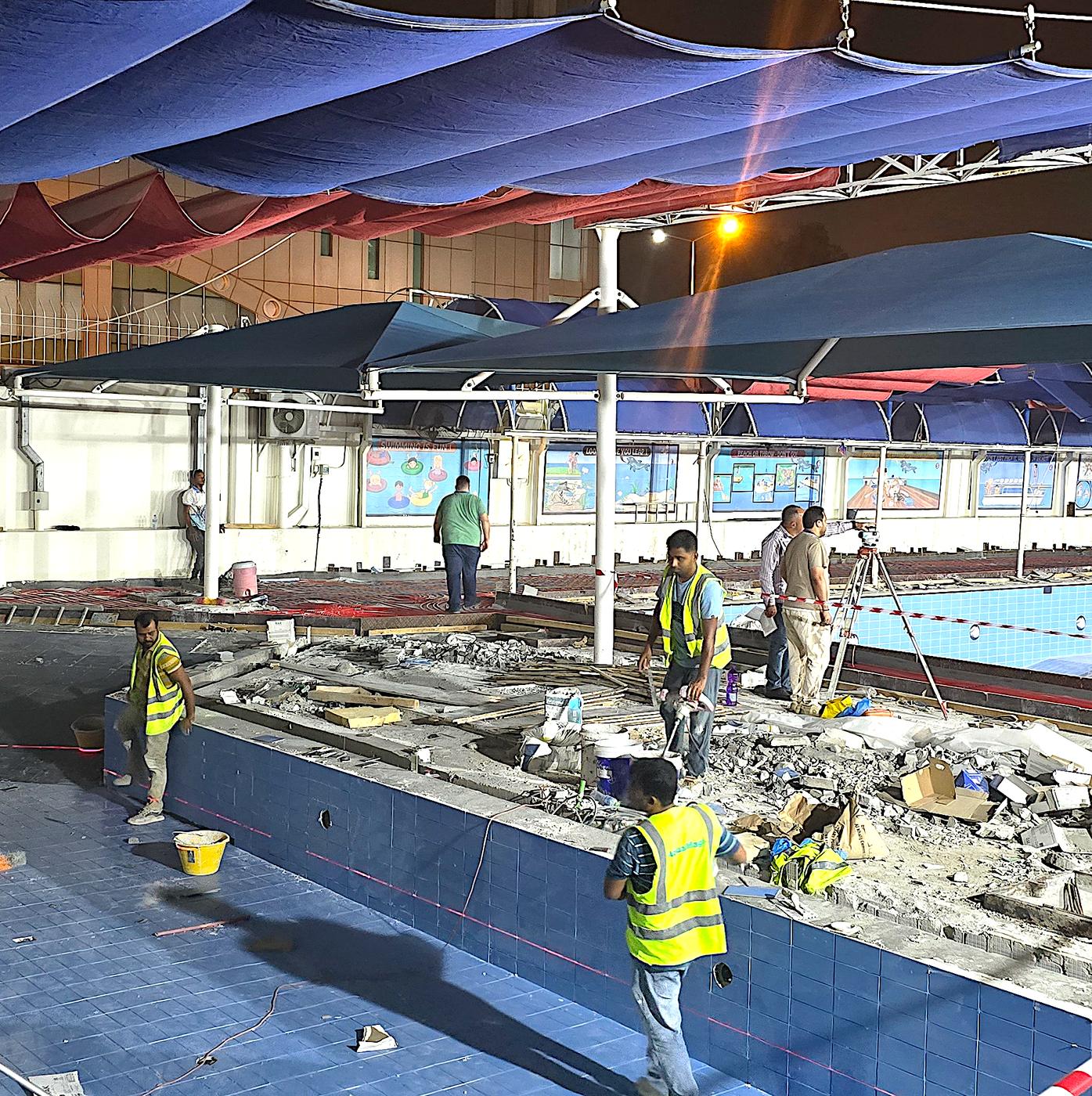 Workers in high-visibility vests resurfacing a pool deck