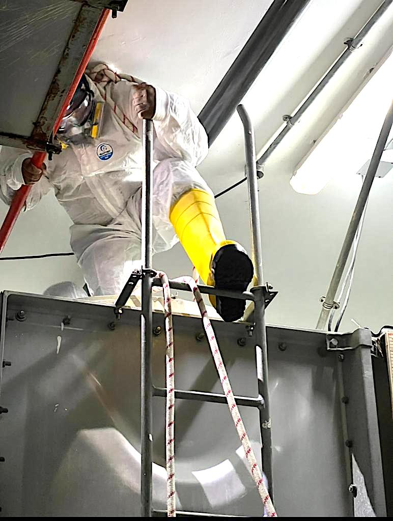 Technician in protective suit climbing into a water tank