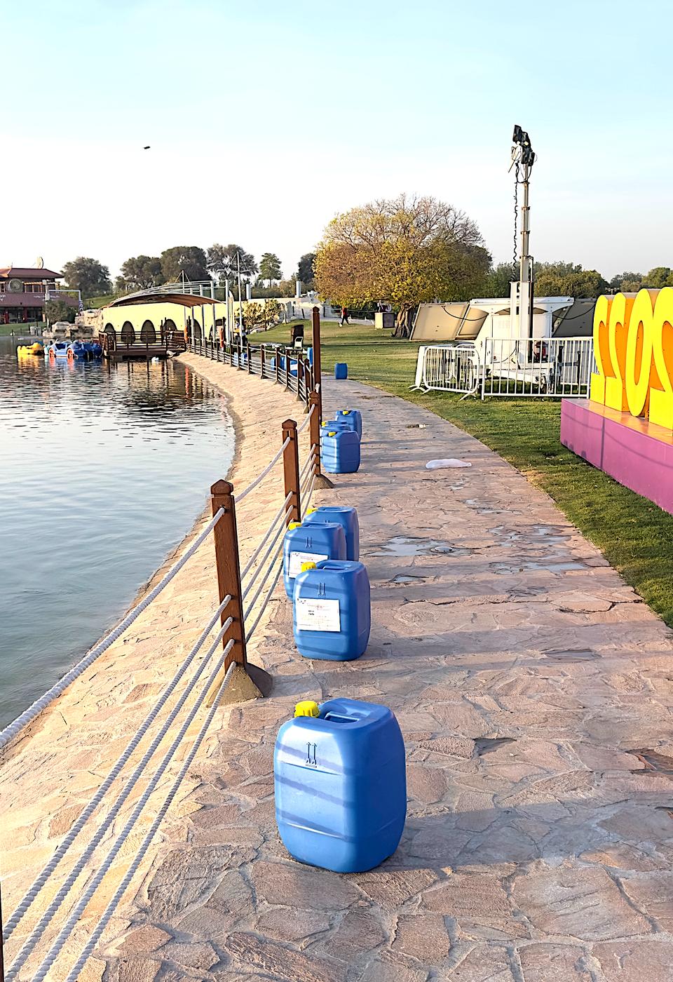 Treated lake with chemical containers lined along a paved waterside path